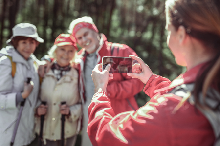 Taking photo. Young lady taking photo on her phone while her parents posing for her at forestの写真素材