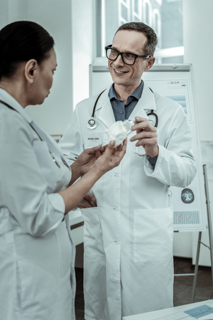 Heart model. Smiling medical specialist with his colleague nearby consulting about future operation with heartの写真素材