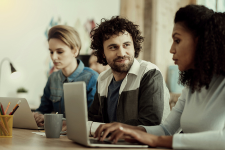 Pleasant talk. Dark-haired handsome office worker with a beard looking interested while talking to...