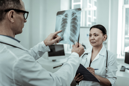 Helper carrying tablet. Interested traumatologist pointing on the x-ray photo showing place of...