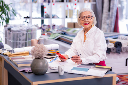 Designer office. Cheerful alluring senior manager in trendy clothing, glasses and golden earrings sitting at her stylish office deskの写真素材