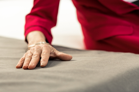 Hand on the sheets. Close-up picture of sophisticated aging lady hand lying on soft grey bed sheetsの写真素材