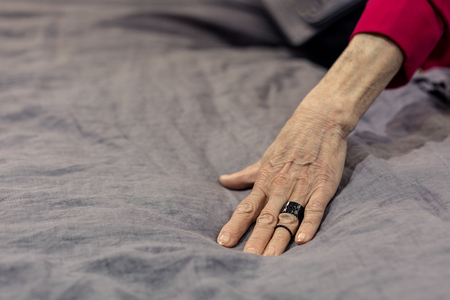 Hand on bed. Mug shot of aging madam graceful hand with massive black trendy ring on grey bed sheetingの写真素材