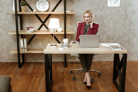 Having conversation. Serious attentive business woman having call related to her work while sitting...