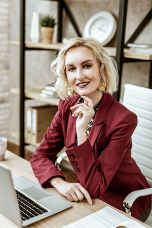Bold dark lipstick. Coquettish short-haired woman with intense makeup working in office while wearing burgundy long jacketの写真素材