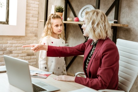 Interfering during conference. Angry strict mother pointing on exit while her little daughter disturbing her during important video sessionの写真素材