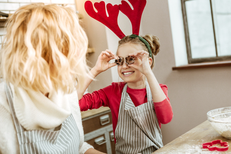 Specious kitchen. Little child with wide smile putting metal form for baking in eyes socketsの写真素材