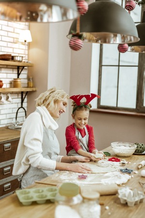 Standing with impatience. Curious pretty girl peeking into hot own and her baking cookies while mother sitting near itの写真素材