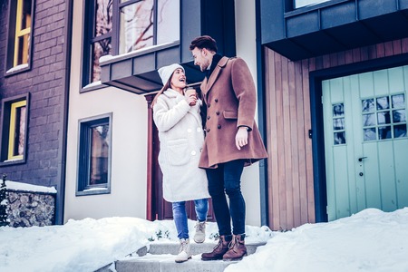 Talking at man. Happy girlfriend holding coffee talking to her handsome man while leaving private houseの写真素材