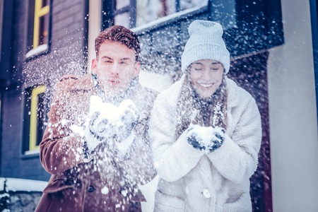 Coats and gloves. Couple wearing warm coats and gloves playing with snow in their residential areaの写真素材