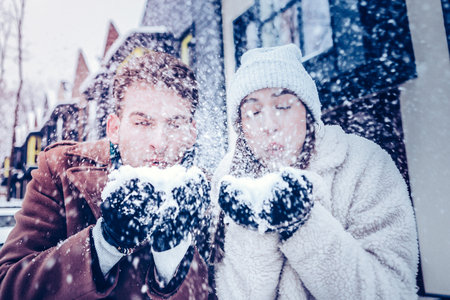 Blowing much snow. Young loving couple loving winter blowing much snow while walking outside the houseの写真素材