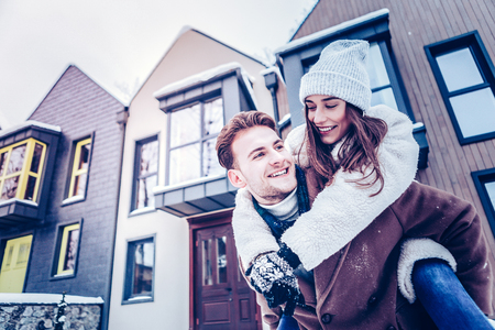 Jumping on back. Cute lovely wife jumping on back of her strong handsome husband walking outside in winterの写真素材