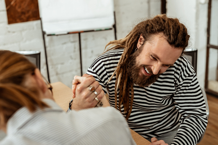 Favourite activity. Joyful bearded man smiling while doing armwrestling with his colleagueの写真素材