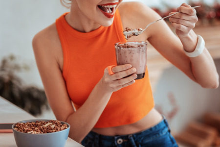 So appetizing. Joyful nice woman holding a glass with muesli while eating themの写真素材