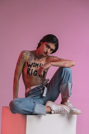 On the pedestal. Young brunette pretty half-naked model wearing blue jeans sitting on the pedestalの写真素材