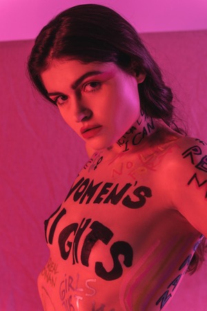 Attentive eyes. Beautiful dark-haired naked model with inscriptions on her breast looking...