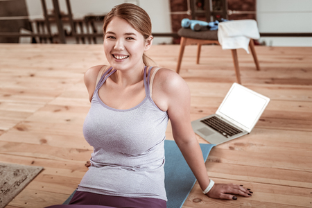 Training actively. Sportive young woman being thirsty after exercises at home and drinking water from plastic bottleの写真素材