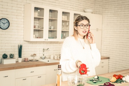 Red bell pepper. Curious talkative woman having conversation through smartphone while having break in cookingの写真素材
