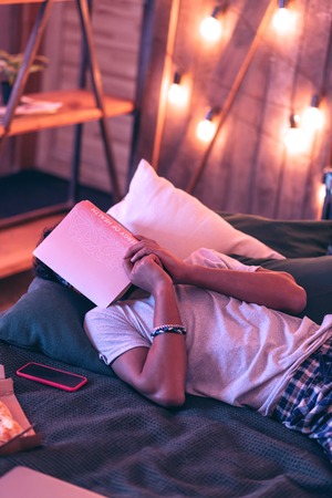 Too exhausted. Active nice boy falling asleep in bed while reading a book because of fatigue.の写真素材