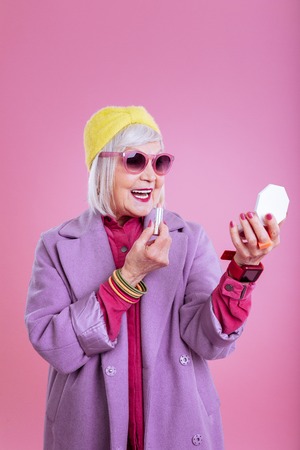 Pink lips. Beautiful fashionable retired woman with pink lips and pink sunglasses coloring her lipsの写真素材