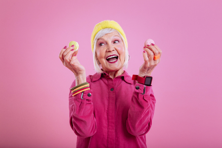 Yummy macarons. Retired woman feeling extremely excited holding two sweet yummy macaronsの写真素材