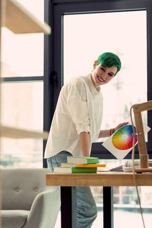 Color choice. Nice joyful woman looking at the color wheel while choosing the colour for her projectの写真素材