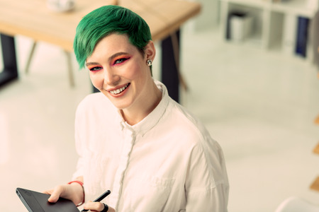 Optimistic mood. Delighted beautiful woman smiling to you while standing with a graphic tabletの写真素材