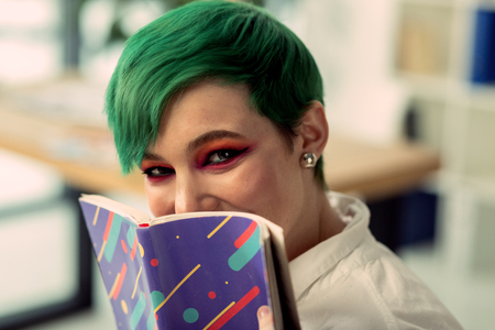 Unusual hairstyle. Portrait of a beautiful green haired woman while holding her bookの写真素材