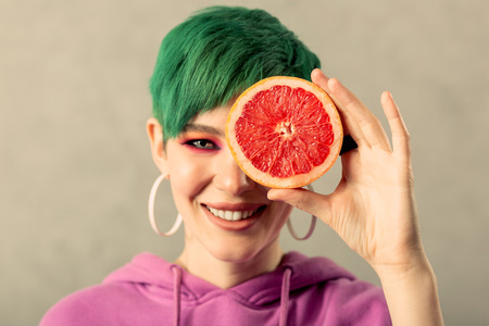 Delicious fruit. Portrait of a beautiful woman smiling while holding a grapefruitの写真素材