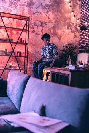 Chatting with girl. Graceful young man sitting on a bar stool with a glass of red wine and talking by video with a girl.の写真素材