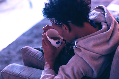 Pleasant smell. Cute boy in the grey hoody warms his hands by fresh tea in polka dot cup.