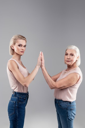 Serious old mother. Peremptory young lady and old grey-haired woman raising hands and connecting...