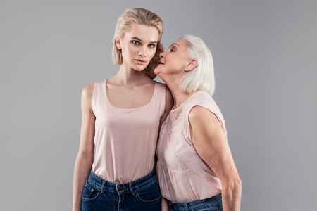 Whispering secret. Interested grey-haired senior quietly sharing secrets with her daughter while she attentively listeningの写真素材