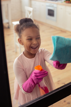 Girl laughing. Funny African-American girl laughing while enjoying helping her mother with cleaningの写真素材