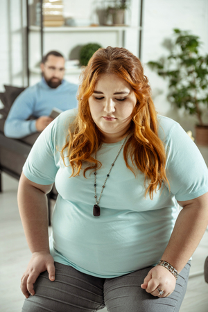 Eating problem. Serious plump woman sitting on the foreground and being in all earsの写真素材