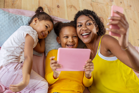 Little beauty. Happy dark-skinned mother keeping smile on her face while doing selfie photo