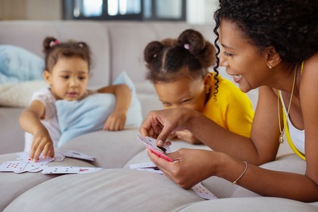 Friendly communication. Positive delighted mommy leaning elbows on sofa and playing cards with her daughtersの写真素材