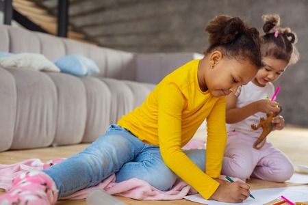 Just imagine. Positive delighted girls sitting on blanket and preparing creative present