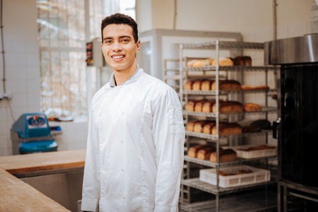 Baker smiling. Young dark-haired professional baker smiling while feeling excited before workの写真素材