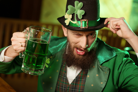 Having fun. Dark-haired bearded young man wearing a leprechaun hat with shamrock having funの素材 [FY310119845171]