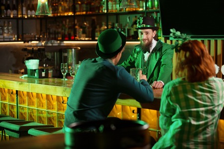 Enigmatic looks. Dark-haired bearded young man in a leprechaun hat looking enigmatic while standing at the bar counterの写真素材