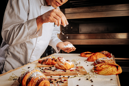 Decorating desserts. Professional young baker standing near oven and decorating pastry dessertsの写真素材