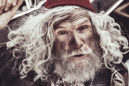 Hi there. Close up portrait of elderly almsman in red beanie whose greeting the passerby.の写真素材