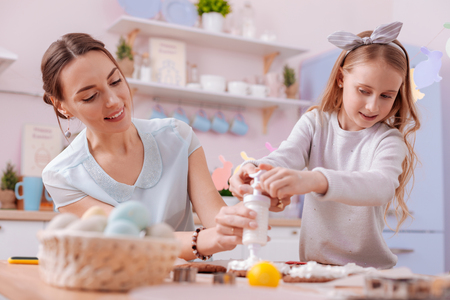 Love sweets. Charming longhaired blonde girl keeping smile on her face looking at cookies
