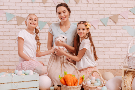 Easter tradition. Charming brunette woman keeping smile on her face while sitting between her daughtersの写真素材
