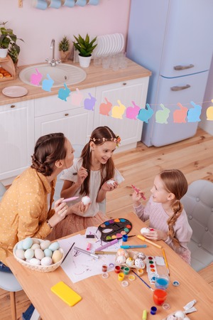 Happy together. Cute young woman listening to her kids and painting eggs togetherの写真素材
