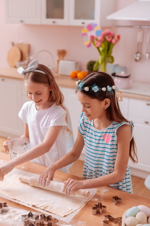 Little helpers. Amazing girls laughing at joke while cooking biscuits togetherの写真素材