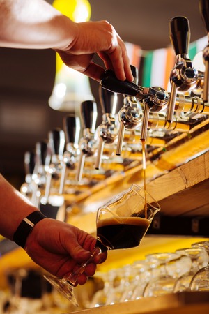 Quality dark beer. Close up of barman pouring quality dark beer into nice glass for his client at nightの写真素材