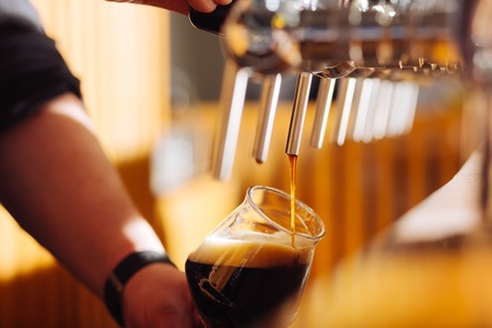 Beer with foam. Close up of barman pouring quality dark beer with foam in the glassの写真素材
