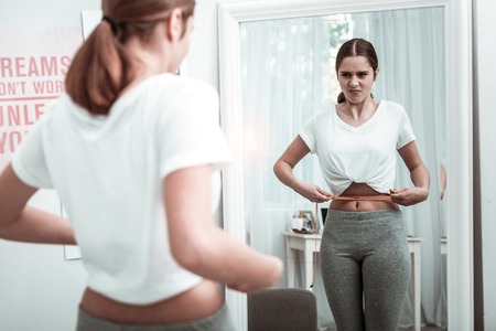 Attitude to own body. A teenage girl looking at her body parameters near the mirrorの写真素材